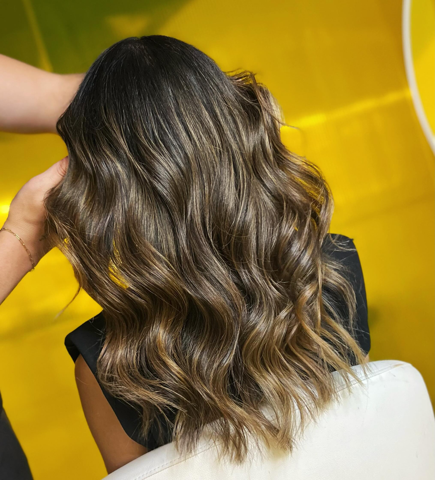 Morena iluminada com balayage caramelo e ondas naturais